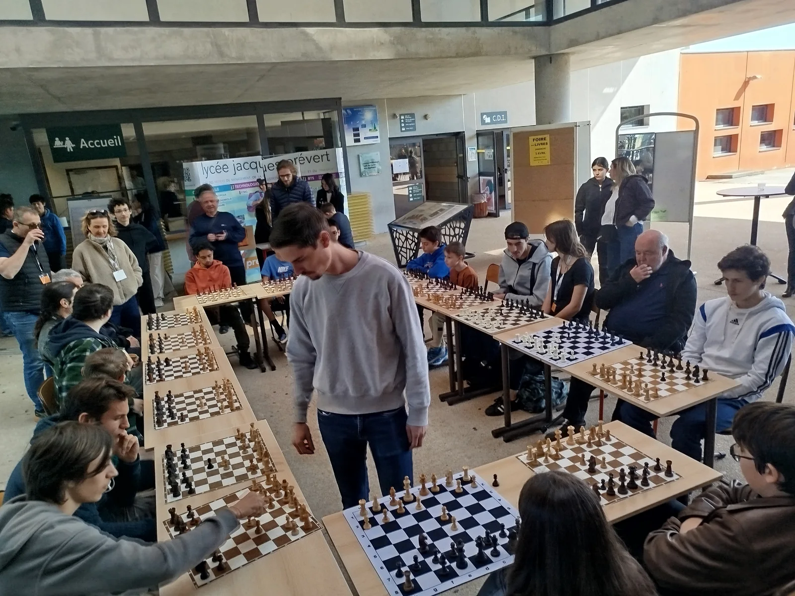 Dans le hall du Salon, des participants et des spectateurs entourent plusieurs tables d’échecs.
